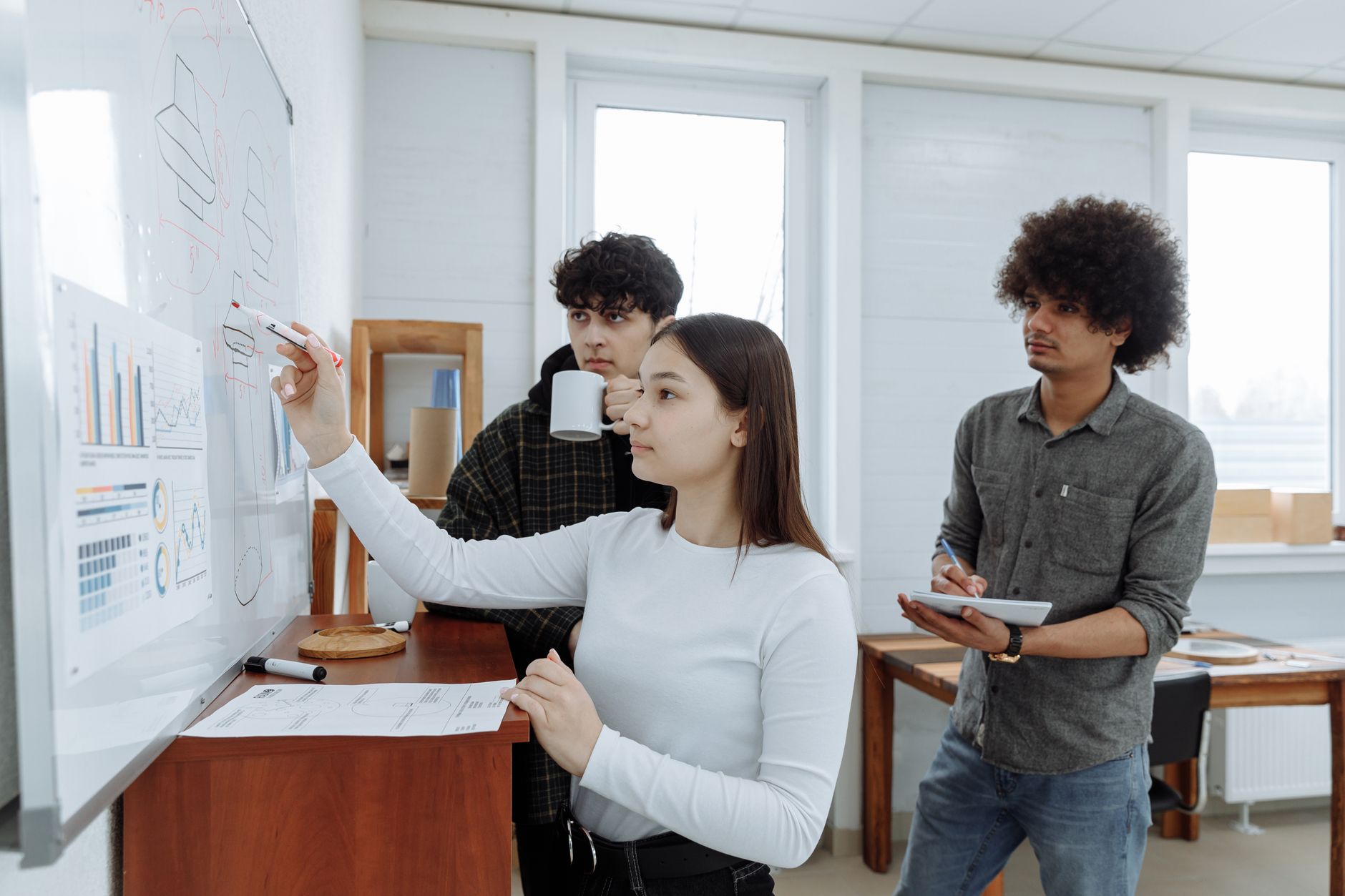 Three team members plan and collaborate at a whiteboard in a modern office setting.