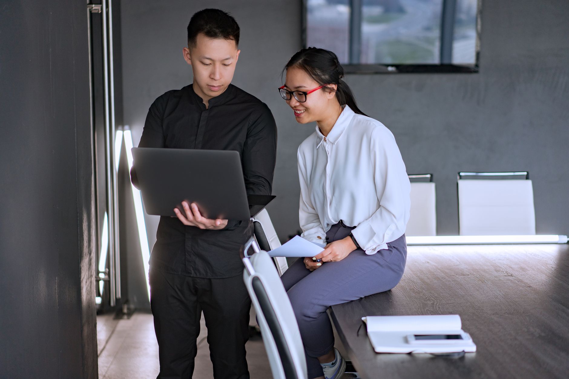 Two professionals collaborating in an office with a laptop, discussing documents and ideas.