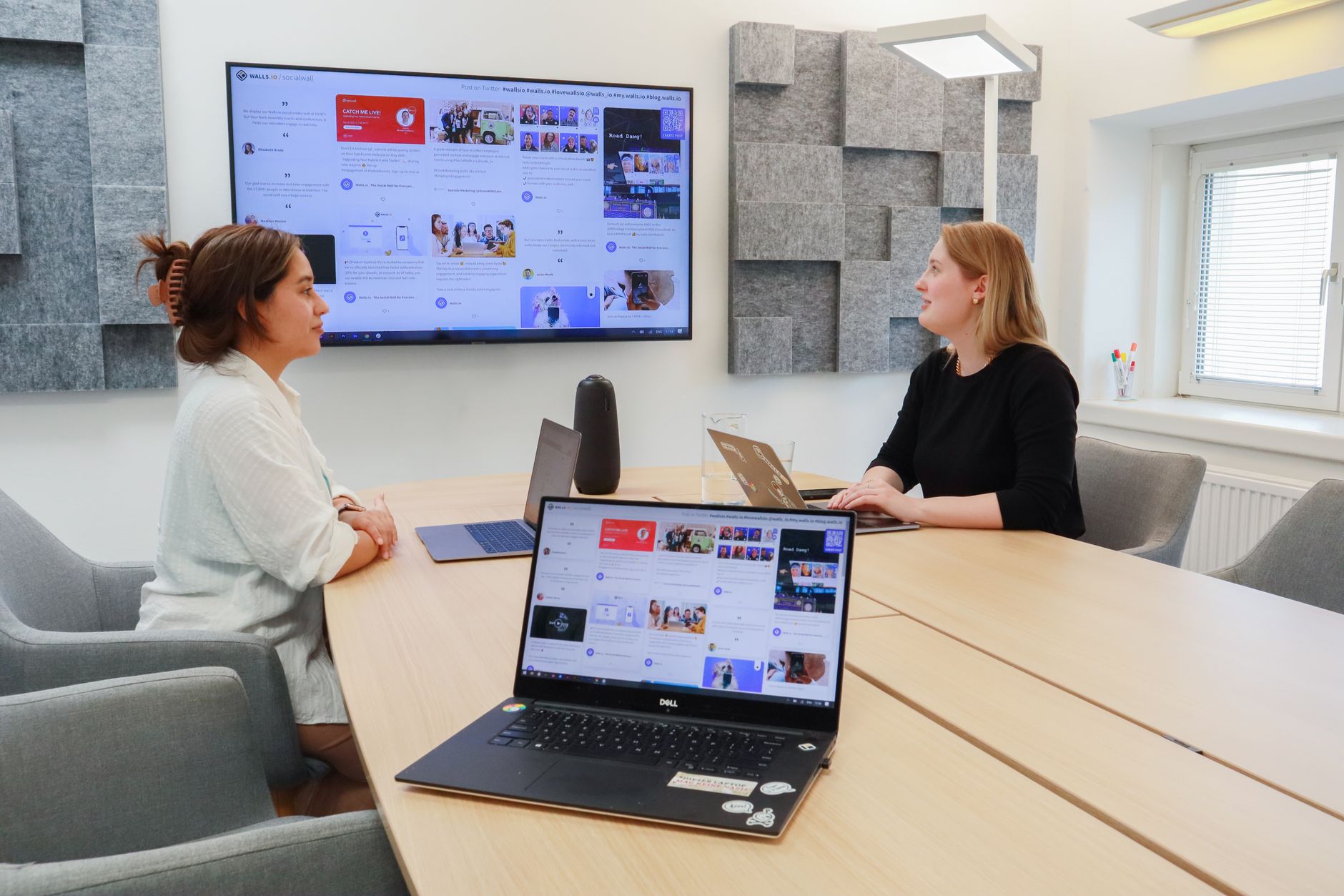 Women collaborating in a modern office with laptops and large digital display.