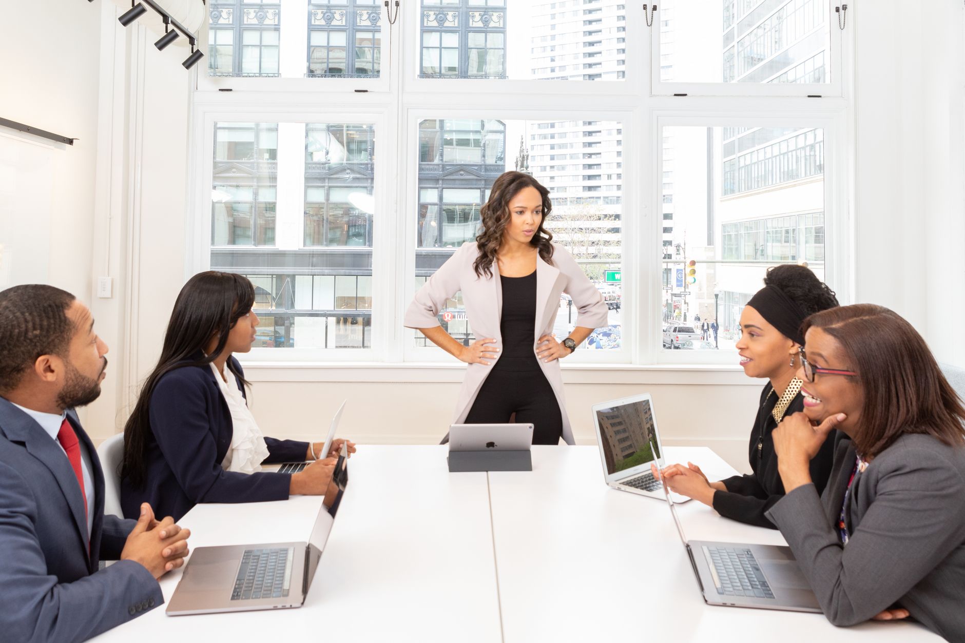 A diverse group of professionals engaged in a meeting at a modern office with laptops and city view.