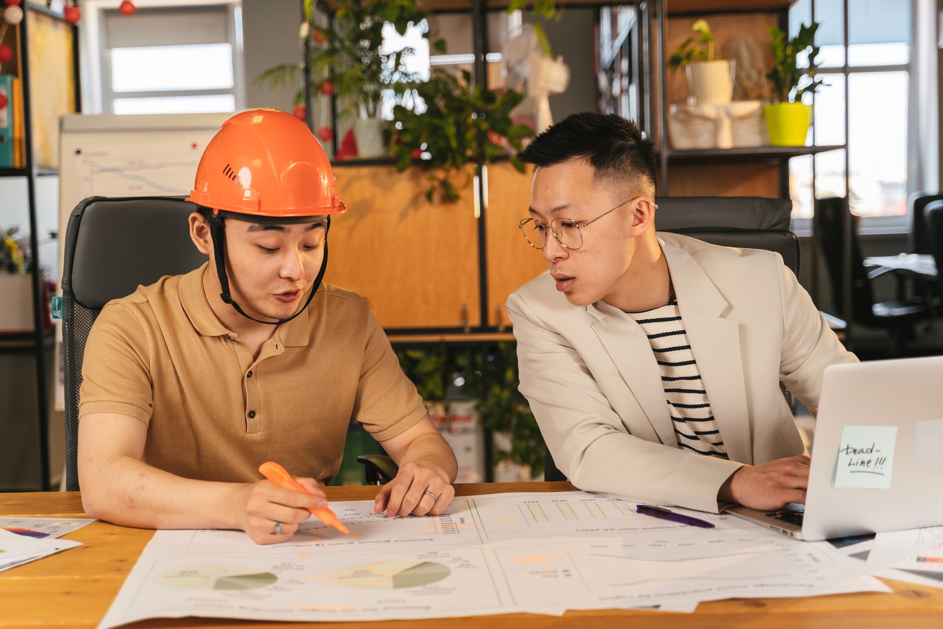 Two men collaborating on project plans in an office setting, reviewing documents on a table.