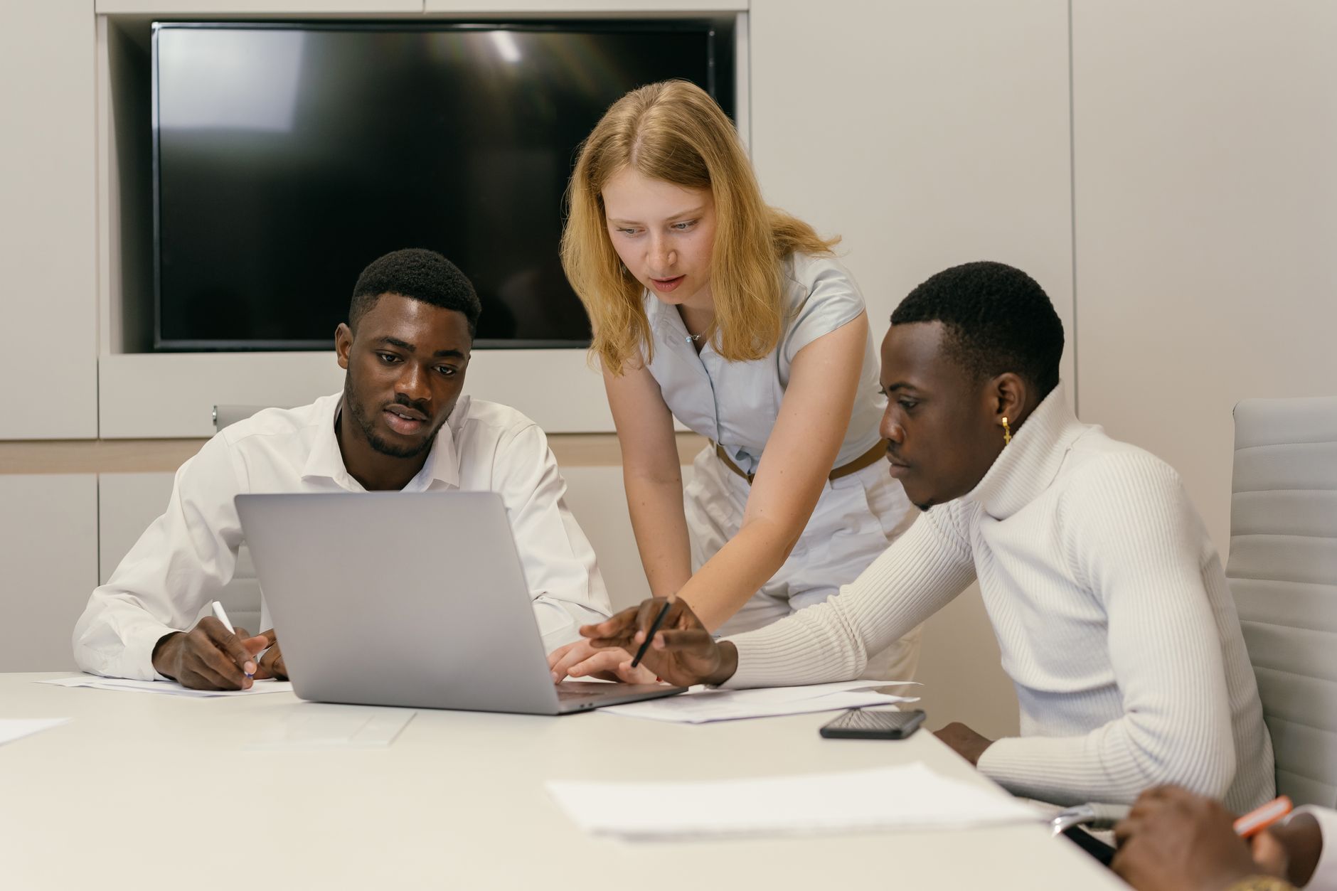 Diverse team working together in a modern office, discussing ideas and collaborating on a laptop.